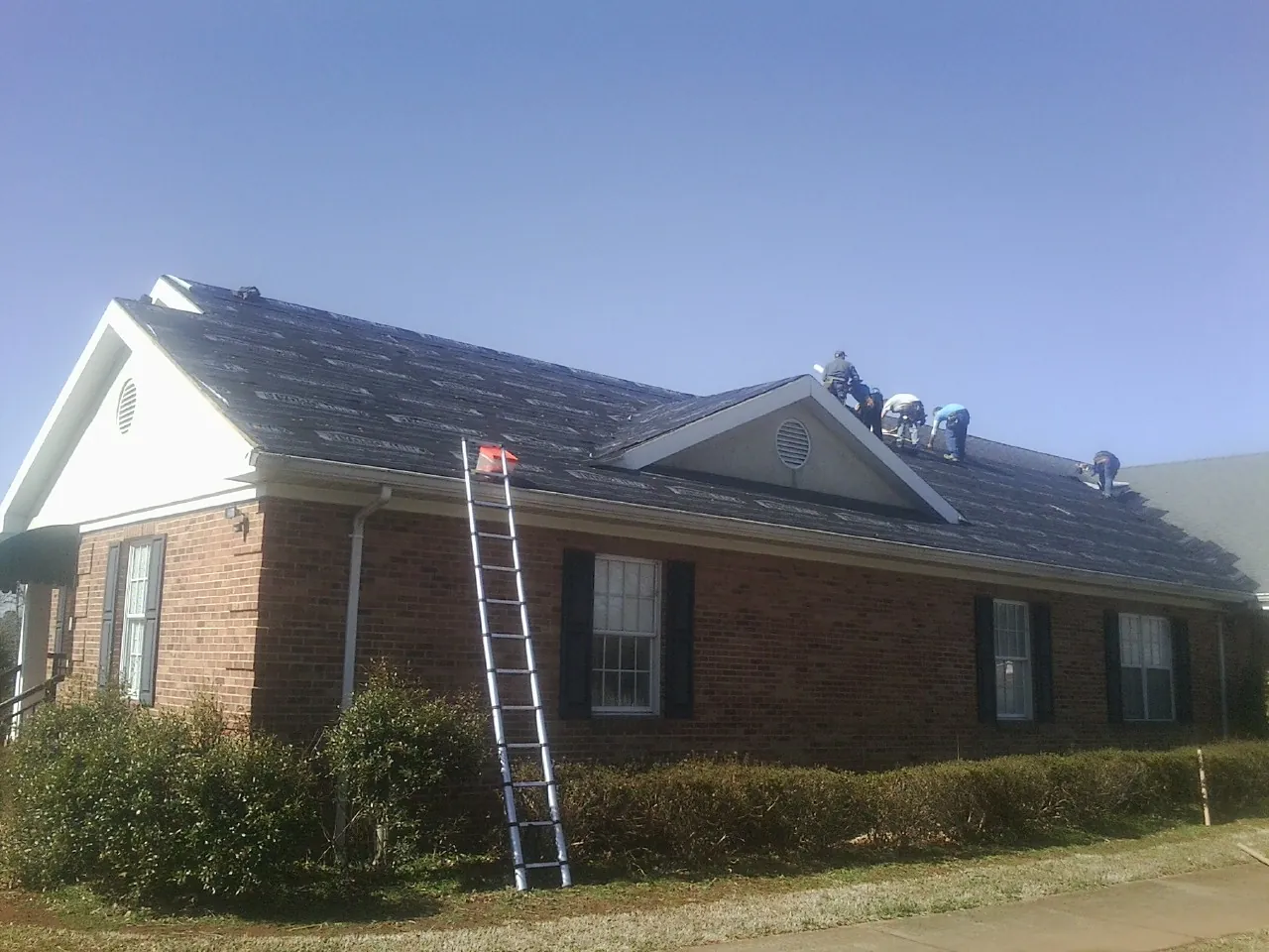 Crew tearing shingles off a brick ranch roof with a ladder set — Metal Roof Repair work by our crew in Smoaks