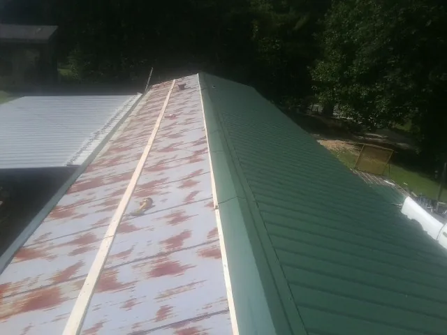 Old rusted panels beside newly installed green metal roofing — Wind Damage Roof Repair by Roofing Brothers in Smoaks