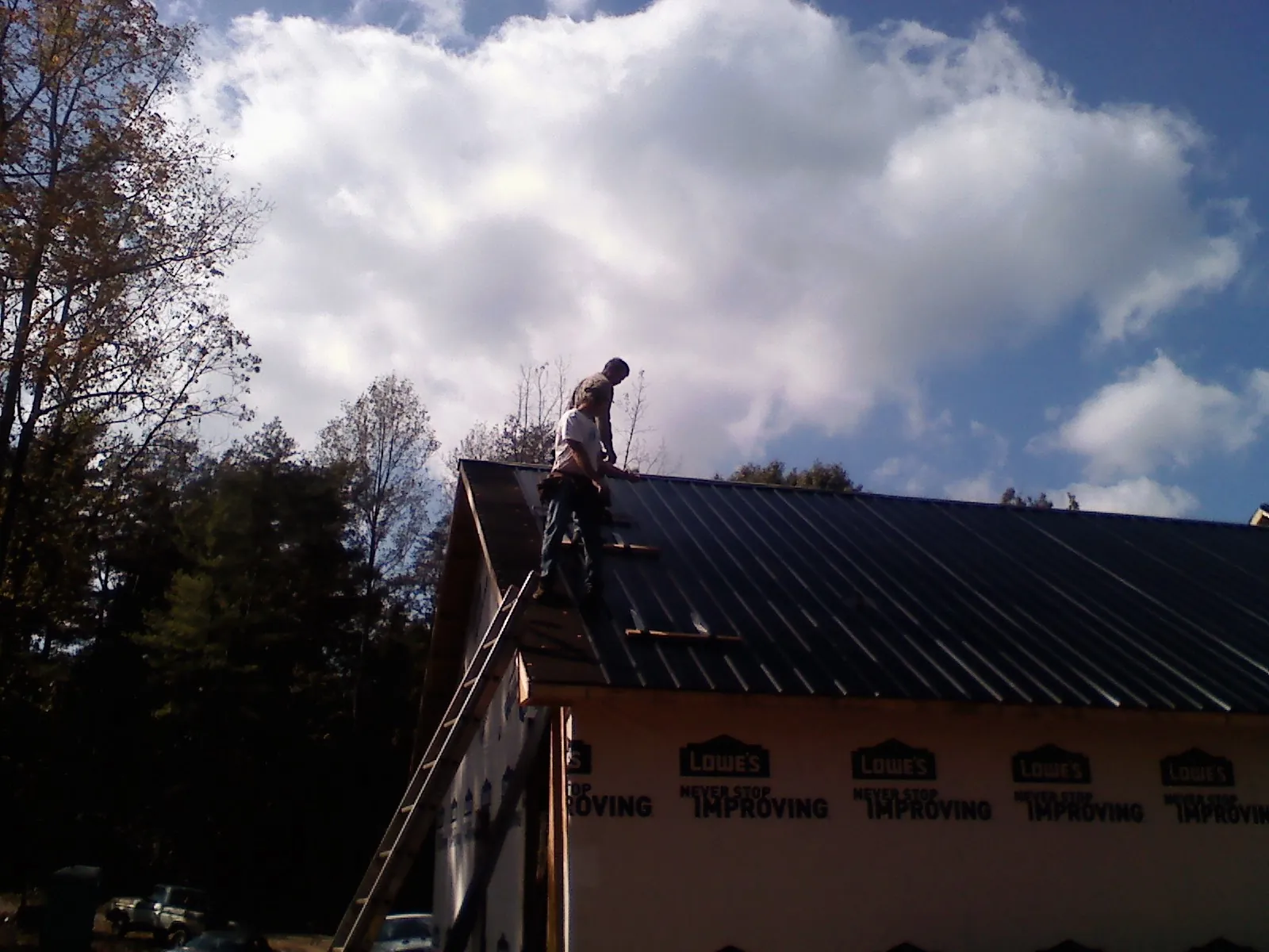 Roofer fastening dark metal panels high against a cloudy sky, from a Roof Inspection job in Smoaks