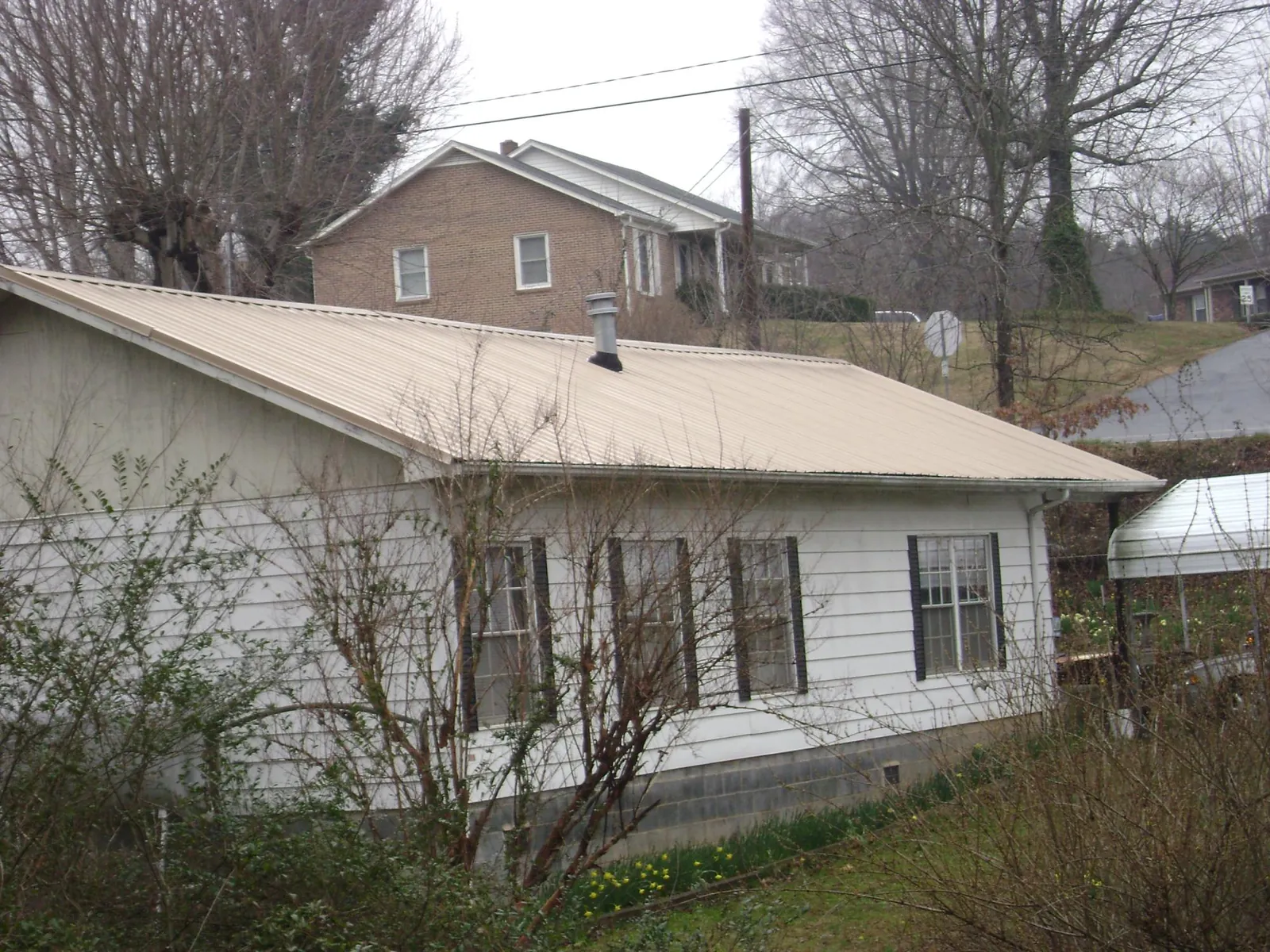 Tan metal roof on a white sided house set into a hillside — Commercial Roofing by Roofing Brothers in Smoaks